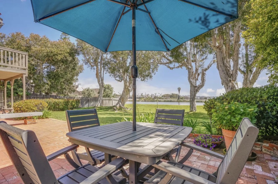 Outdoor dining table under a teal umbrella overlooking the lagoon